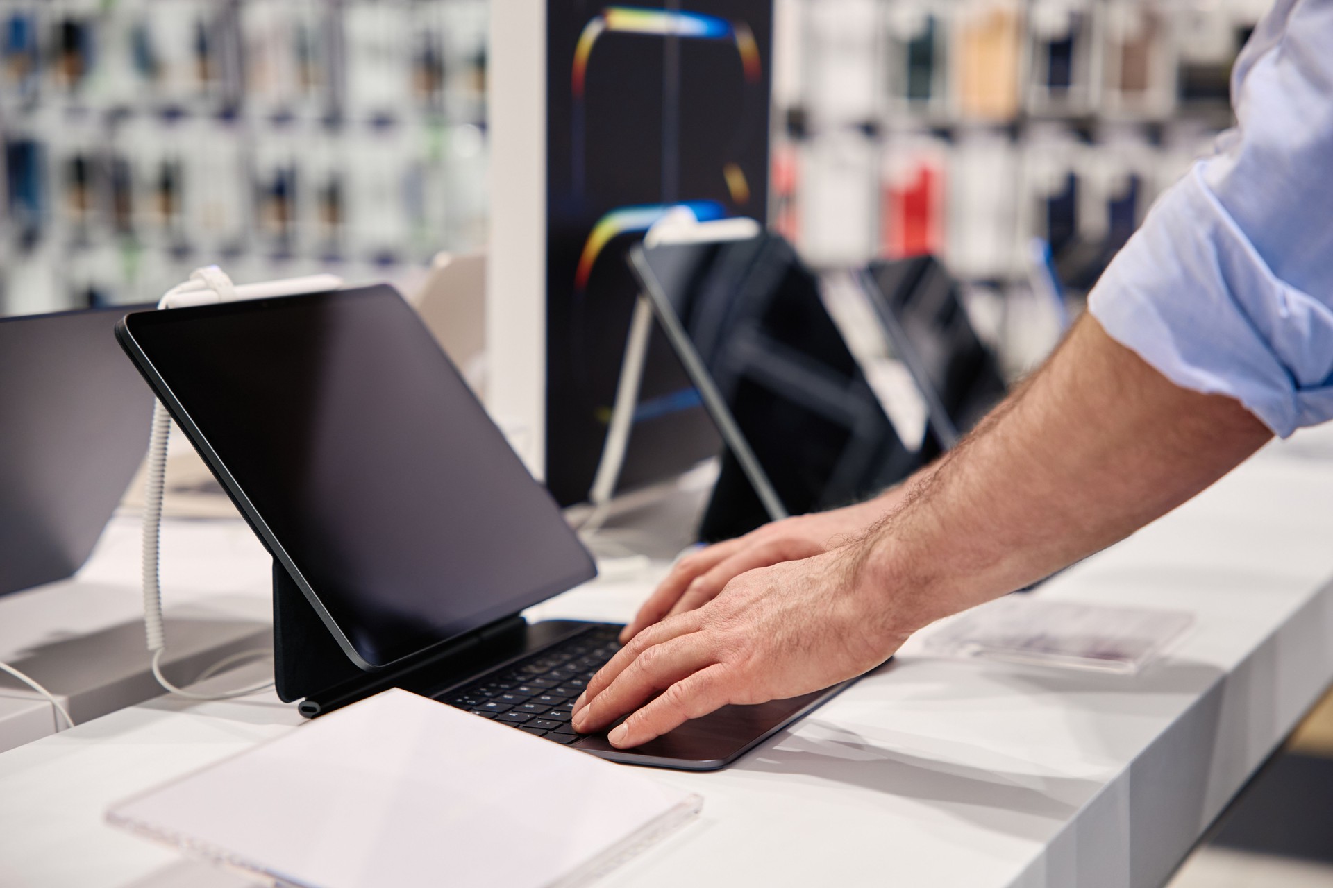 A user interacts with a tablet in a tech store displaying various electronic products