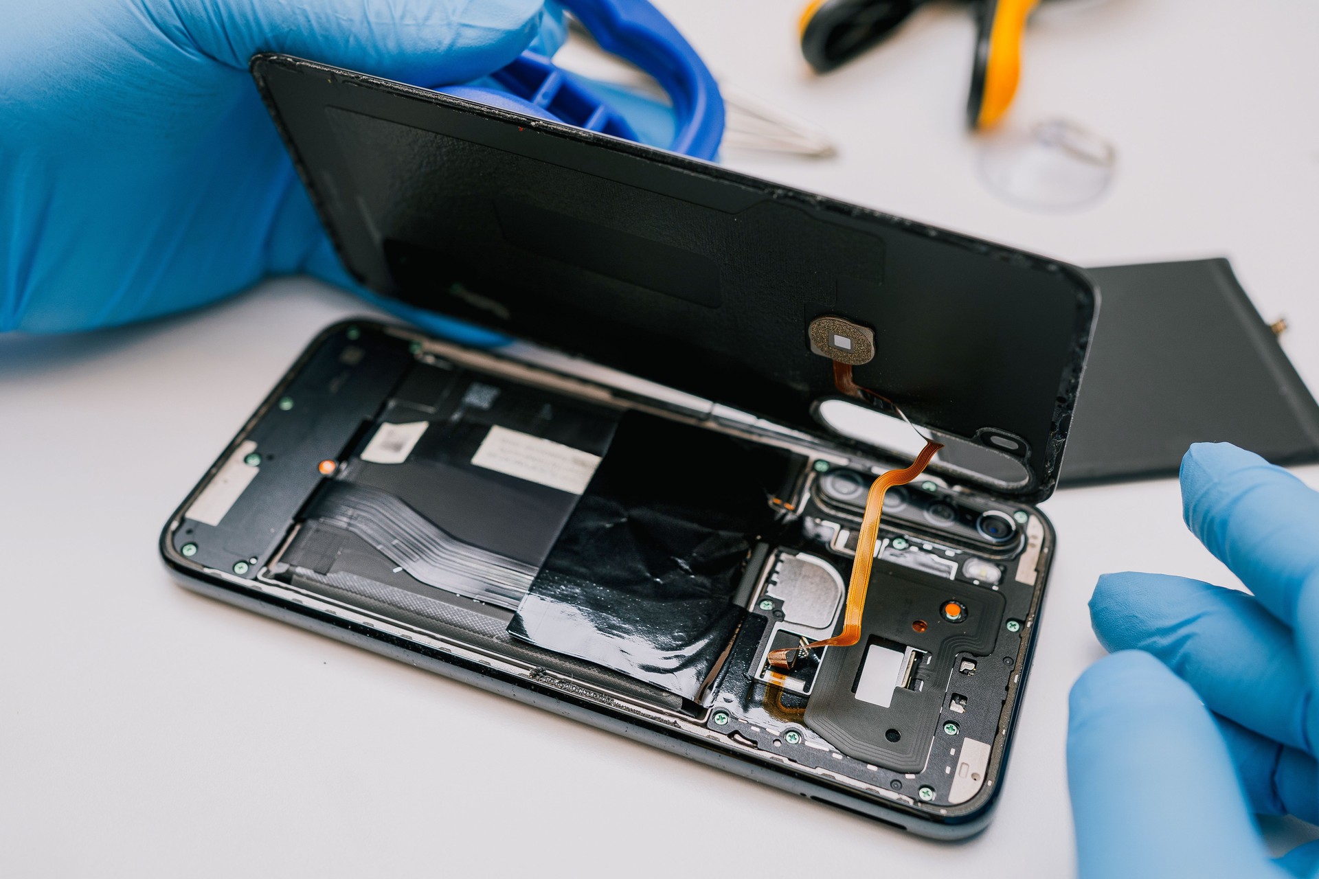 Battery replacement in a mobile phone â a technician in protective gloves disassembles a smartphone, removing the back cover to install a new battery. Repair and maintenance process of electronics.